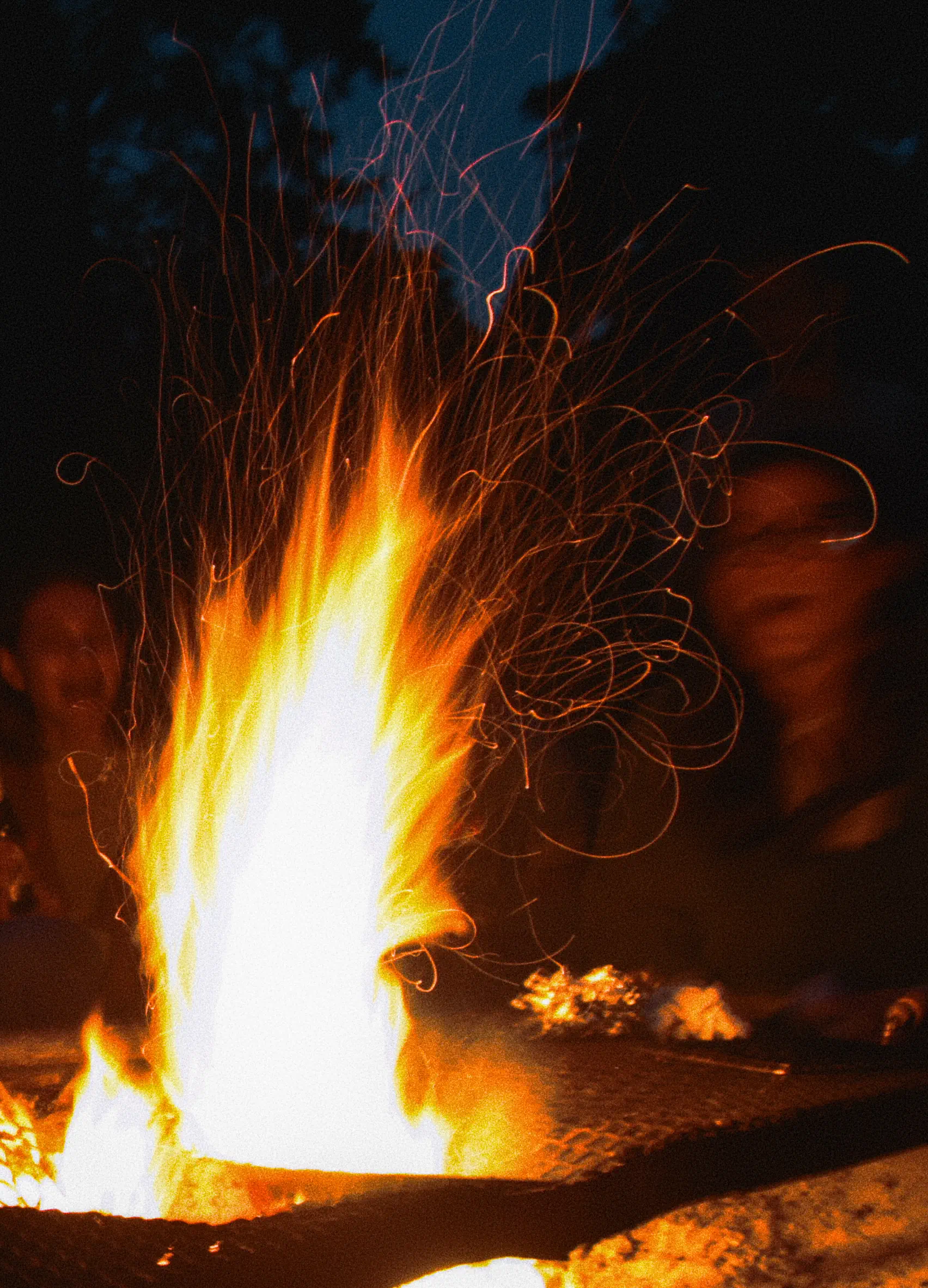 Long exposed flames of a campfire flying through the air, with people laughing behind it