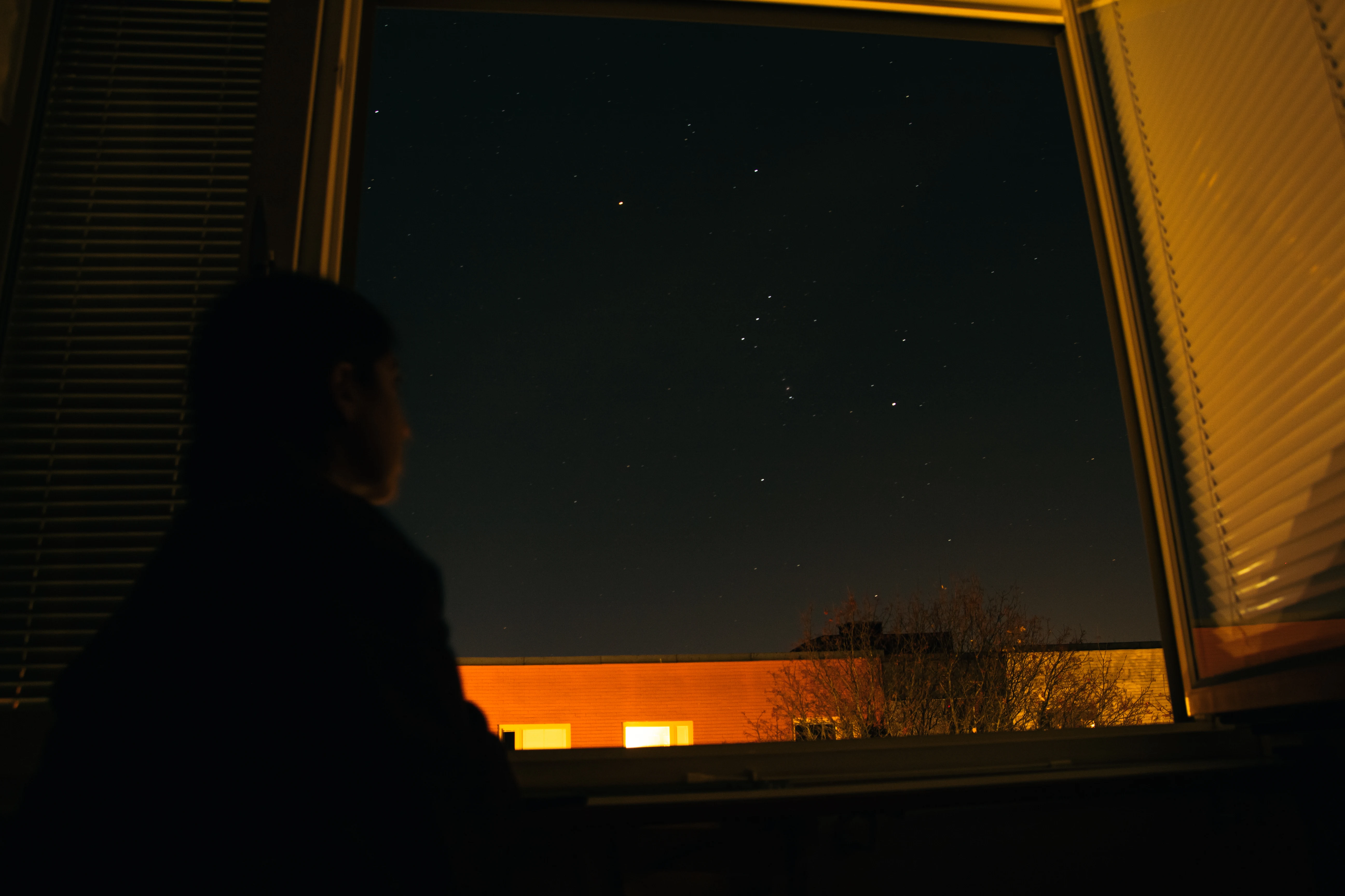 A woman looking at the Orion Constellation from a bedroom window.