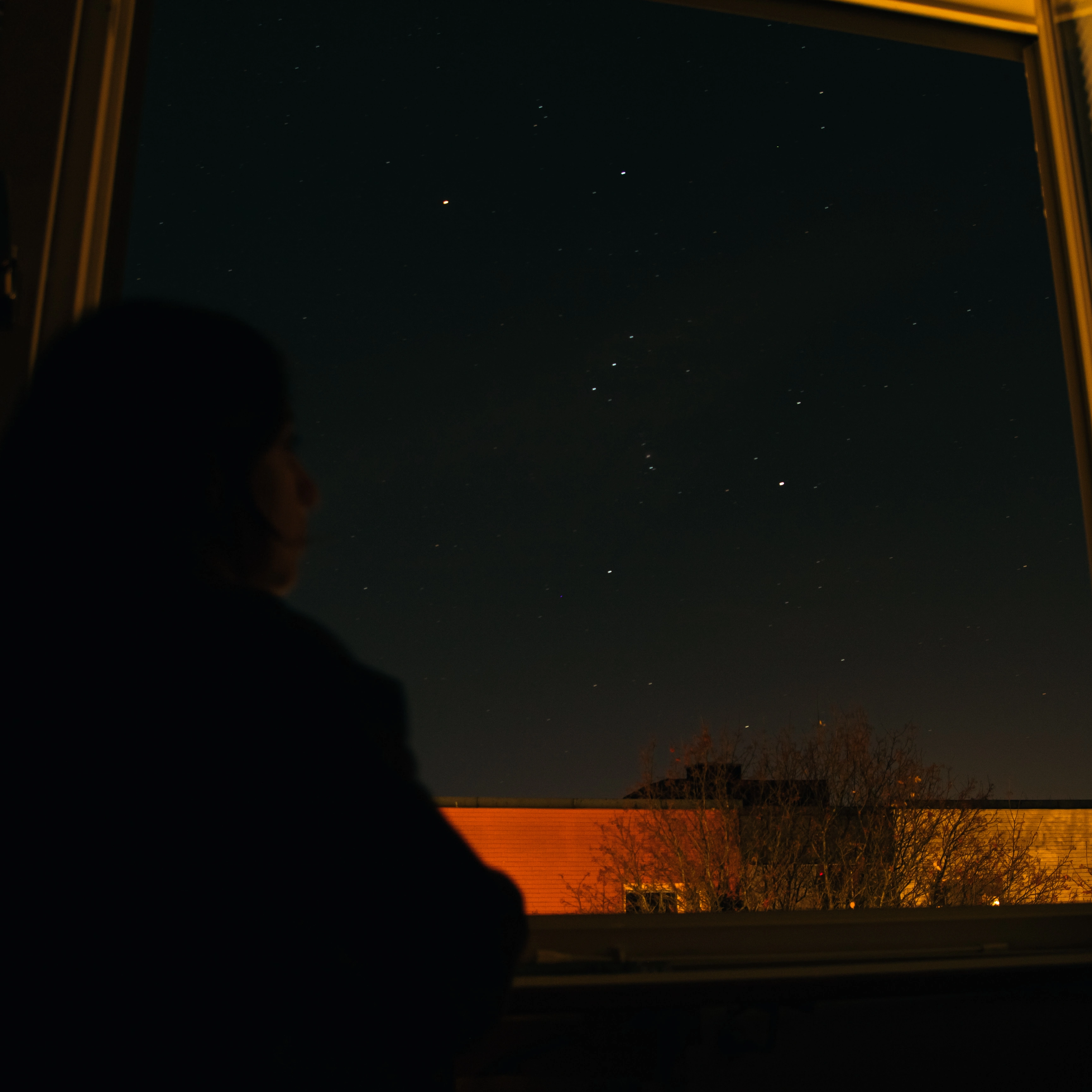 A woman viewing the Orion Constellation from a bedroom window.
