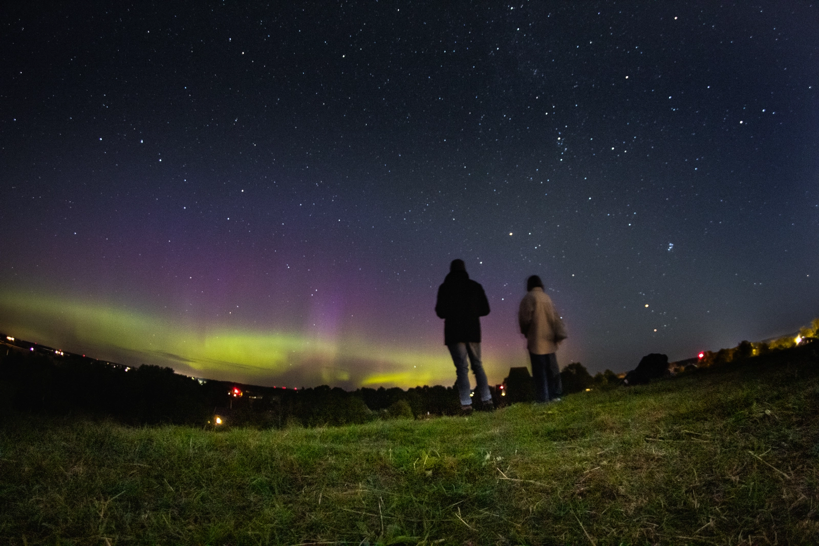 Two people standing on the mound at Gamla Uppsala viewing the Aurora Borealis dancing in the Northern sky.