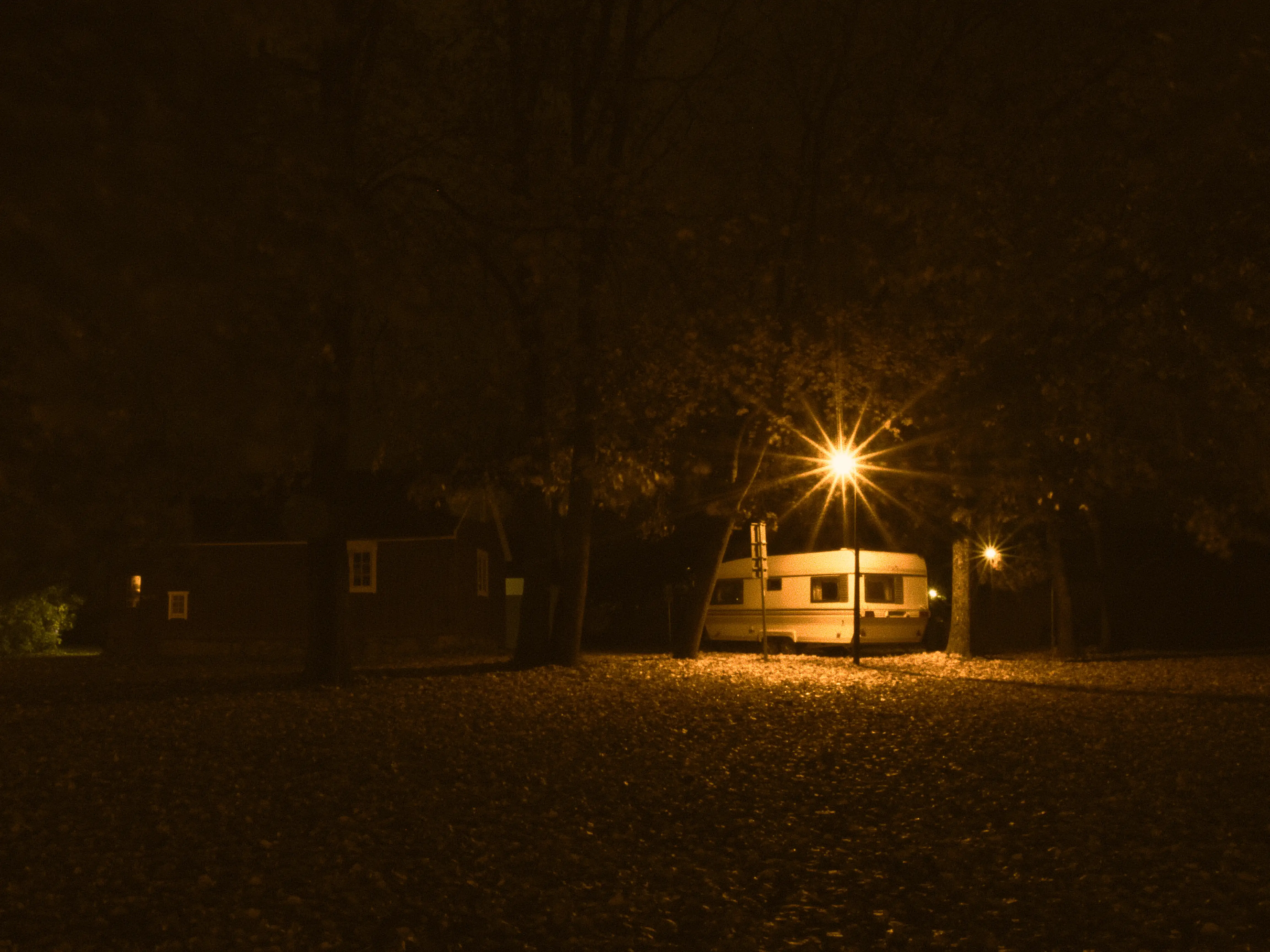 A street light shining through thr cmera lens with a caravan parked behind it.