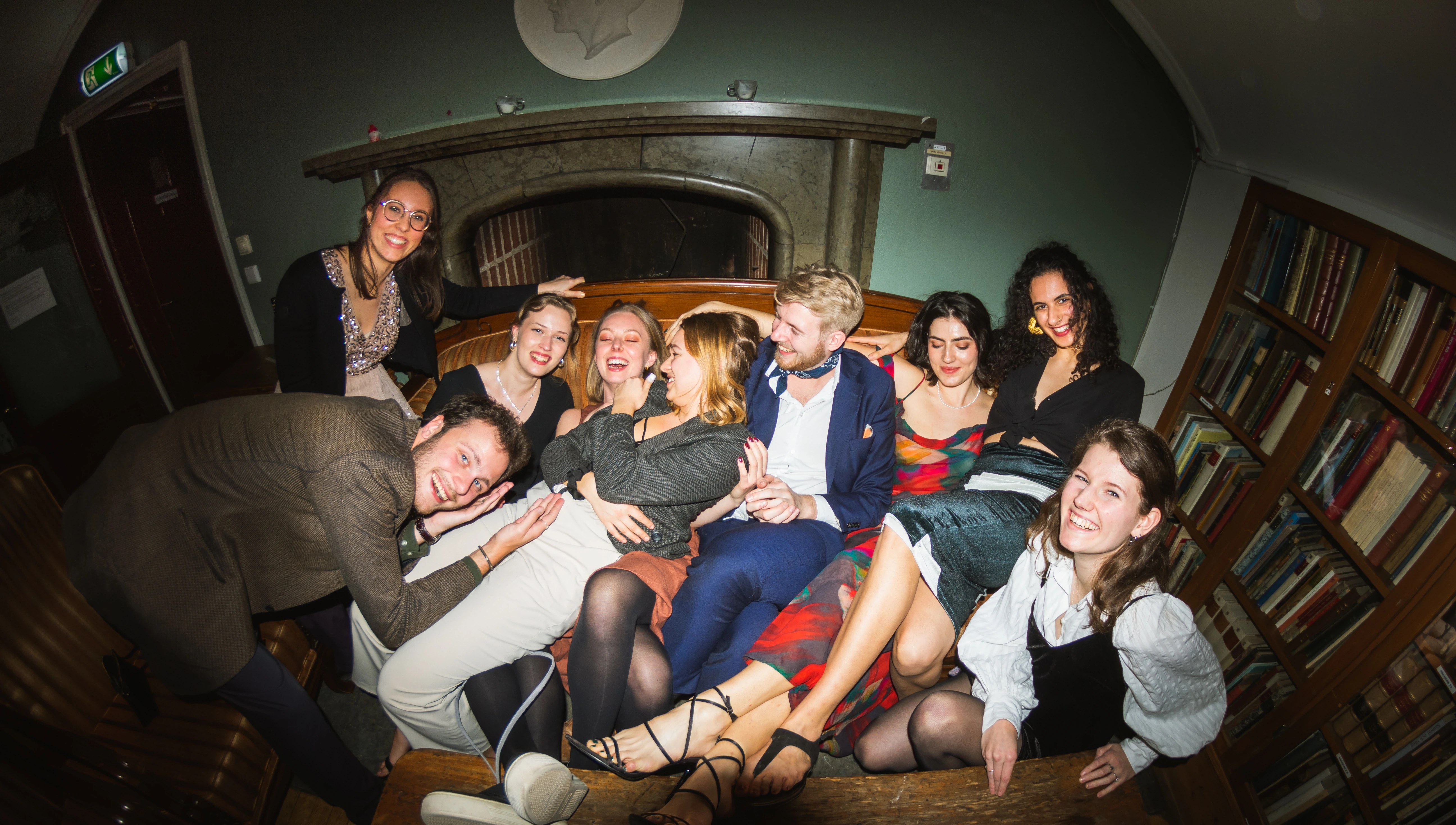 A group of friends sittig on a vintage couch and posing for a photo, at Västgöta Nation, Uppsala.
