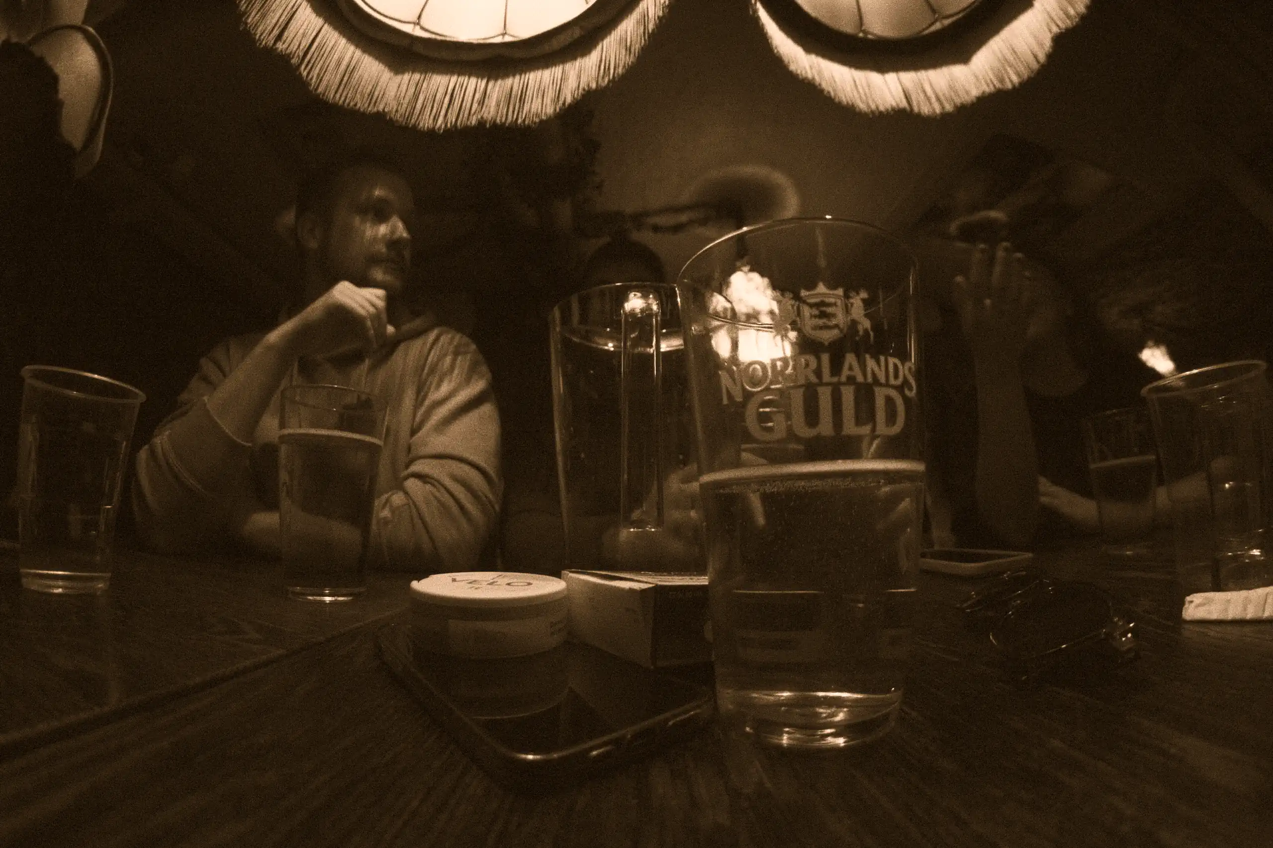 A half filled beer glass with people talking behind it.