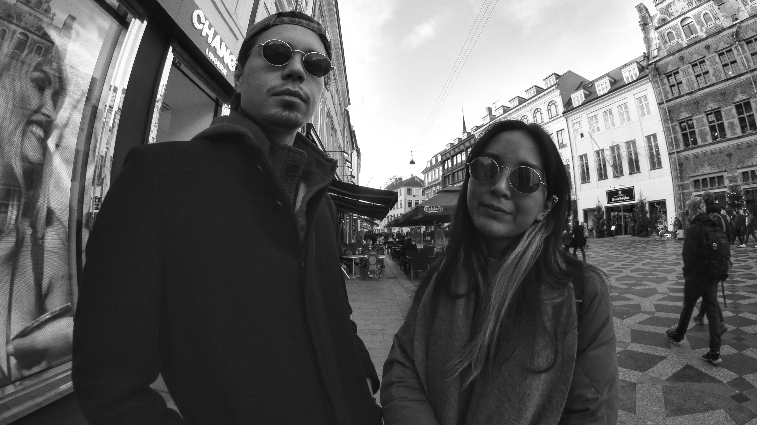A woman and a man, wearing sunglasses, posing looking right at the camera, on the streets of Copenhagen