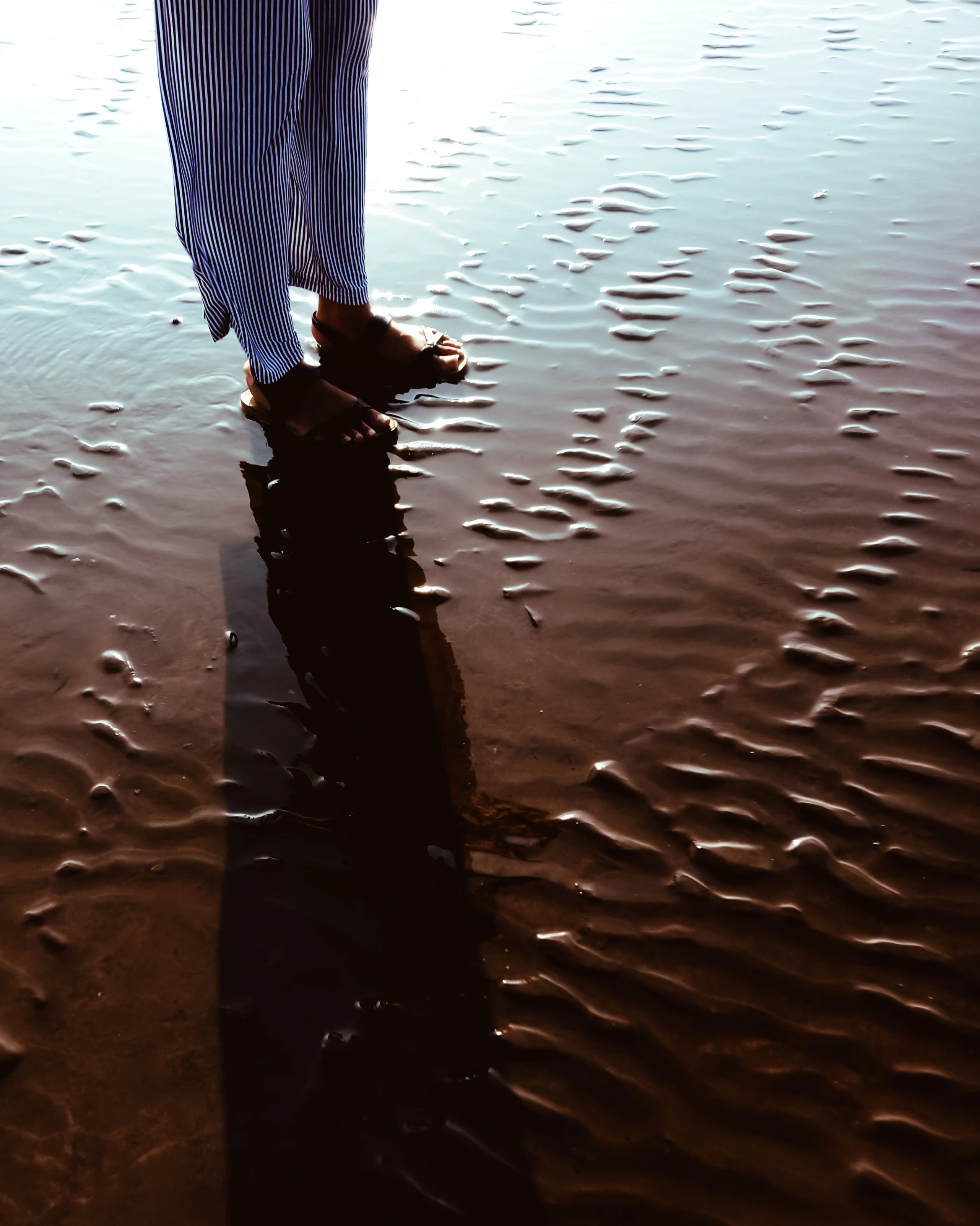 A picture of a woman's legs while she is standig on the wet sand at Gorai Beach, Mumbai