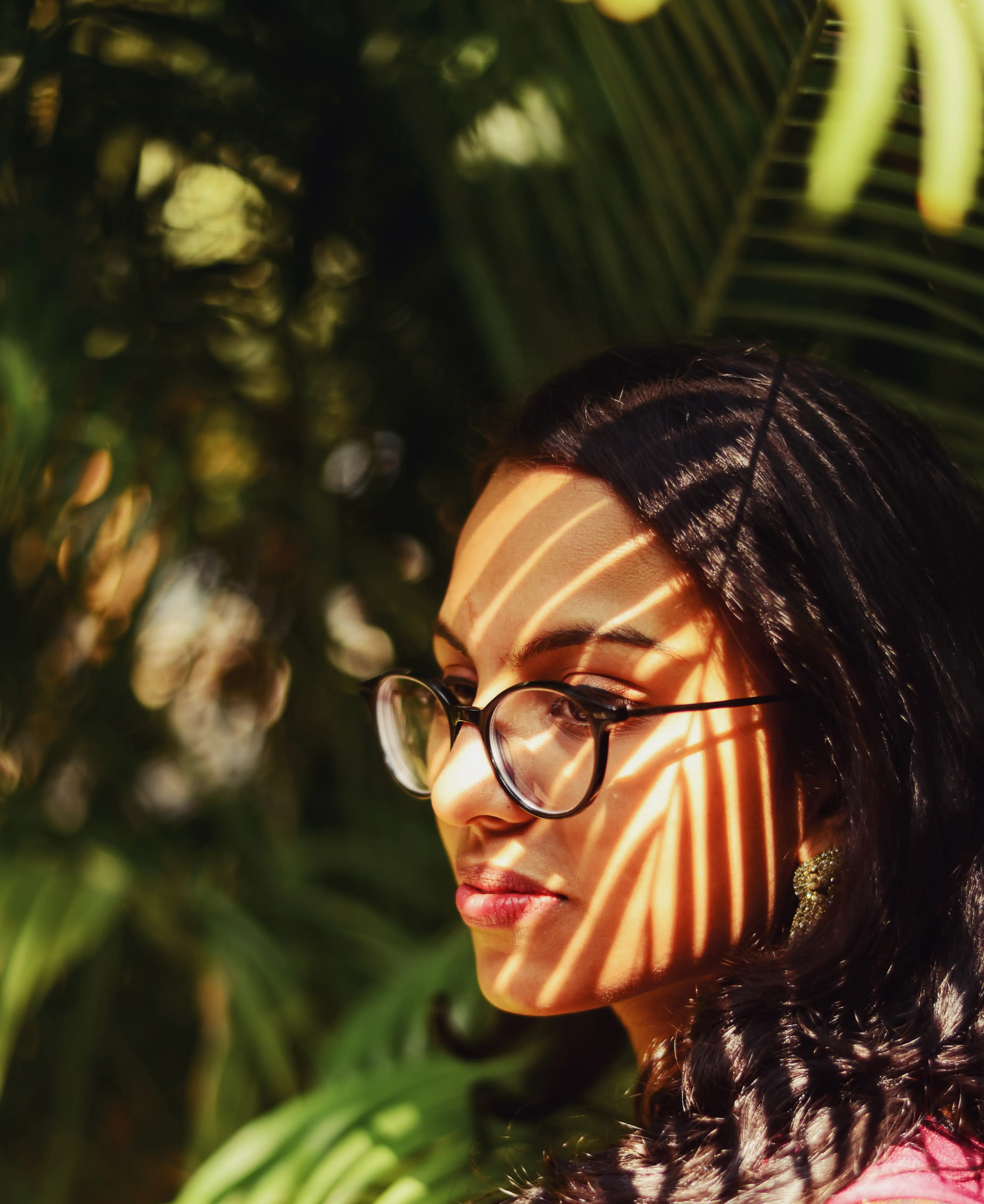 The shadow of a palm tree leaf, on the face of a woman standing under it