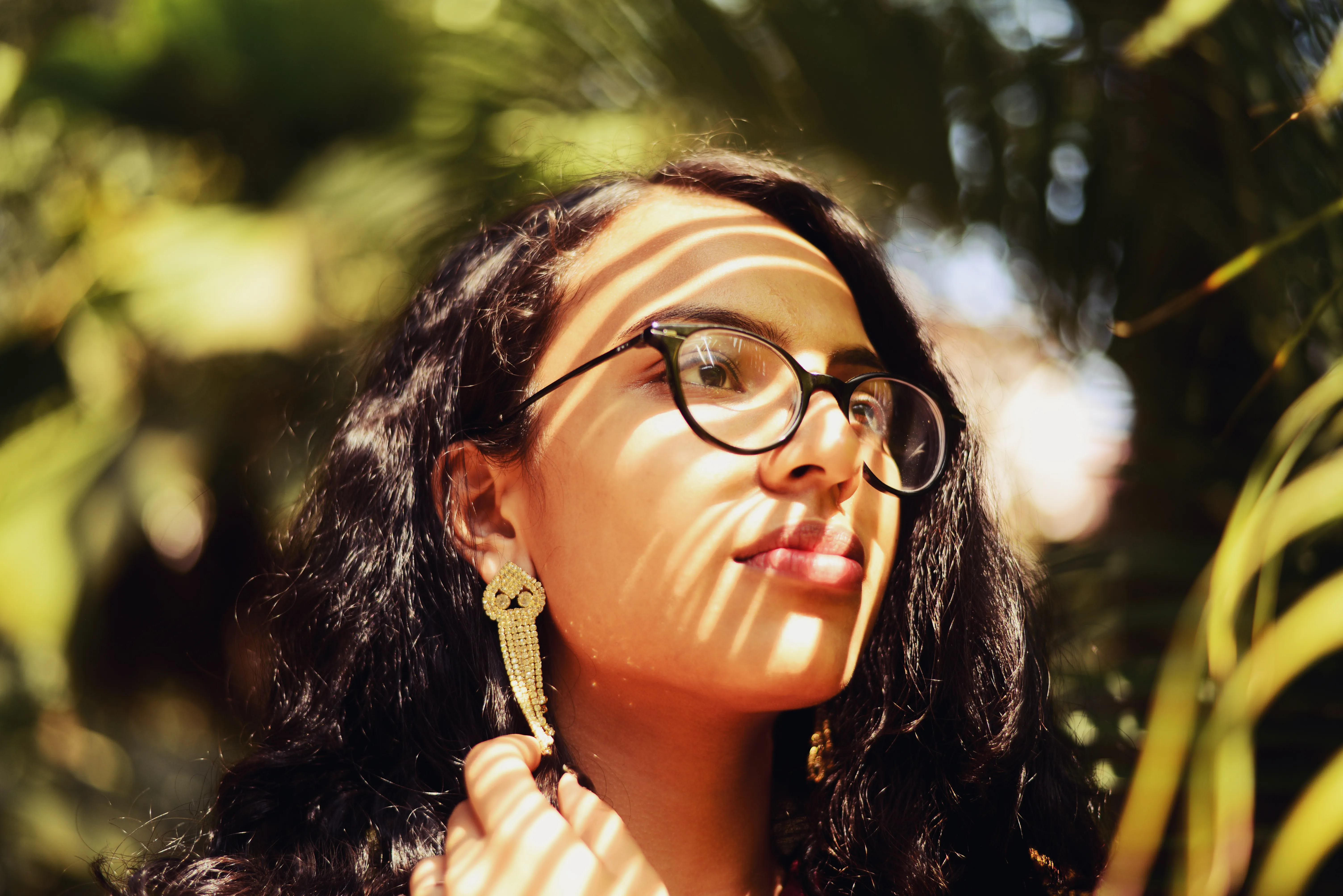 A woman looking forward through palm tree leaves, with the shadows of the leaves projected onto her face